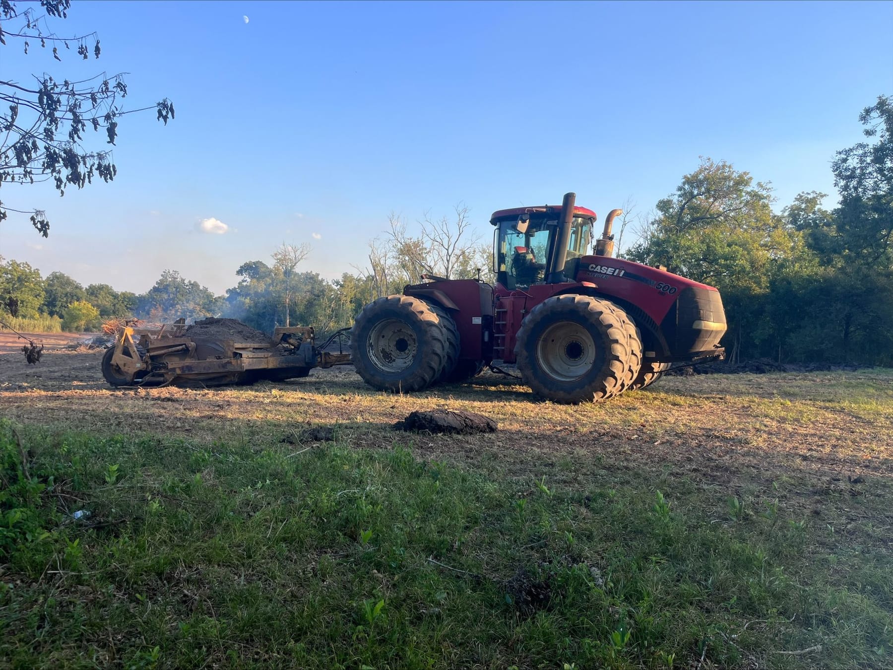 A Case IH Steiger pulling a scraper across a clearing in the evening light.